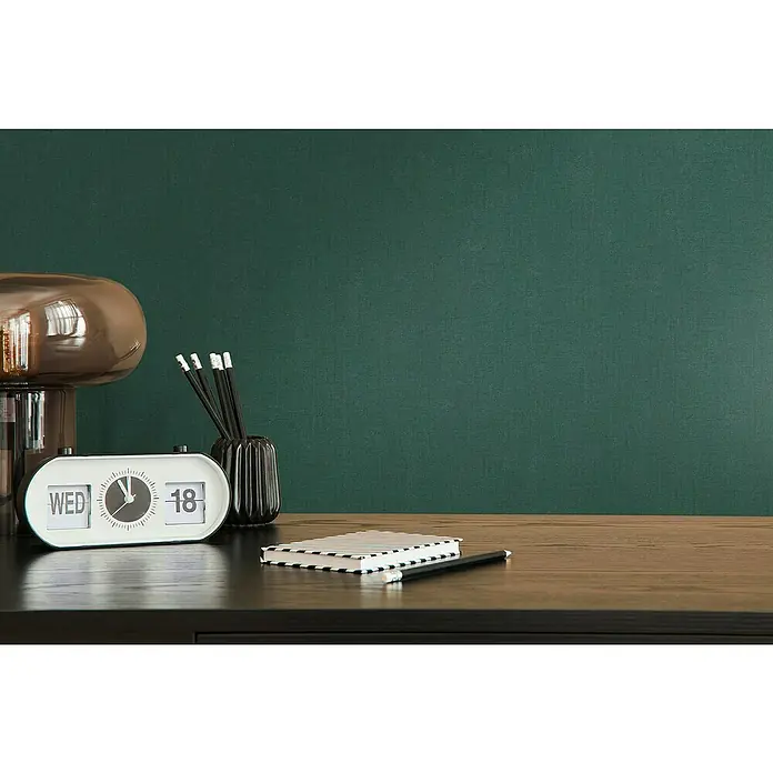 A.S. Création Casual Living Vliestapete - Waldgrün, Uni, 10,05 x 0,53 m - Nahaufnahme eines Schreibtischs mit einem Retro-Flip-Uhr-Kalender, Stiften und einem Notizbuch.