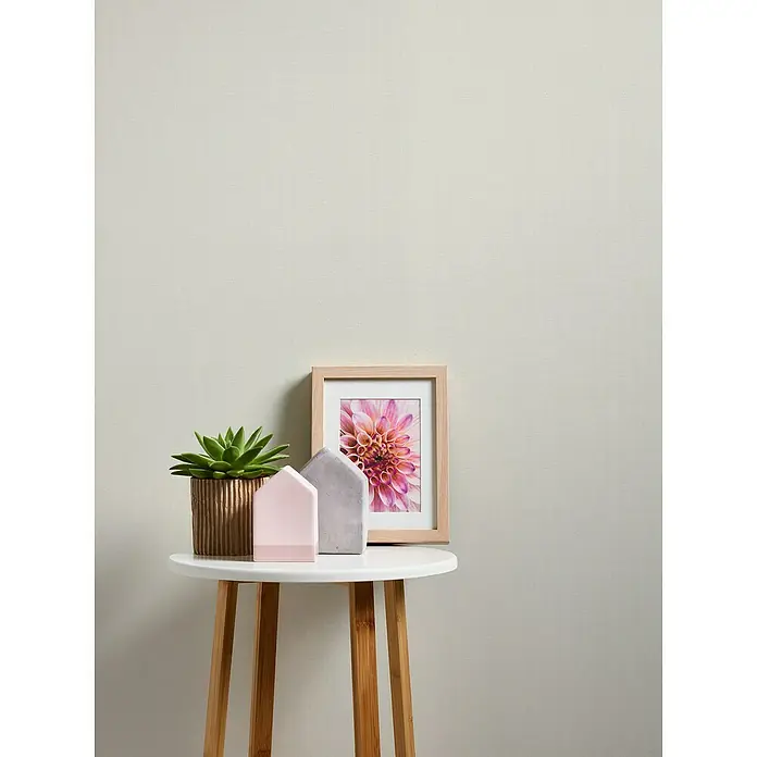 A.S. Création Casual Living Vliestapete Textiloptik - Weiß, Uni, 10,05 x 0,53 m - Dekorative Stillleben-Szene mit Sukkulente, Zierhäusern und gerahmtem Blumendruck auf einem runden Beistelltisch aus Holz, minimalistisch und stilvoll.