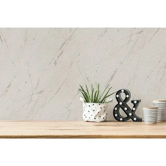 A.S. Création Casual Living Vliestapete Marmor - Silbergrau-Metallic, Steinoptik, 10,05 x 0,53 m - Nahaufnahme eines dekorierten Tisches mit einer Pflanze im Korb, einem beleuchteten "&"-Zeichen und zwei gestreiften Keramikbechern.