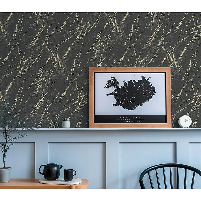 A.S. Création Casual Living Vliestapete MarmorSchwarz/Gold/Metallic, Steinoptik, 10,05 x 0,53 m - Elegantes Interieur mit stilvoller Dekoration: Ein gerahmtes Island-Poster, eine Teekanne, Tasse und eine Uhr auf einem Regal vor einer Wand mit Marmormuster.