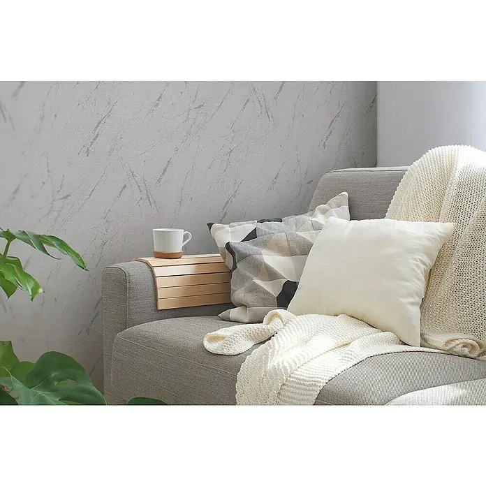 A.S. Création Casual Living Vliestapete Marmor - Silbergrau-Metallic, Steinoptik, 10,05 x 0,53 m - Nahaufnahme eines Sofas mit Kissen, einer Decke und einem Beistelltisch mit einer Tasse darauf, ideal für eine gemütliche Leseecke.