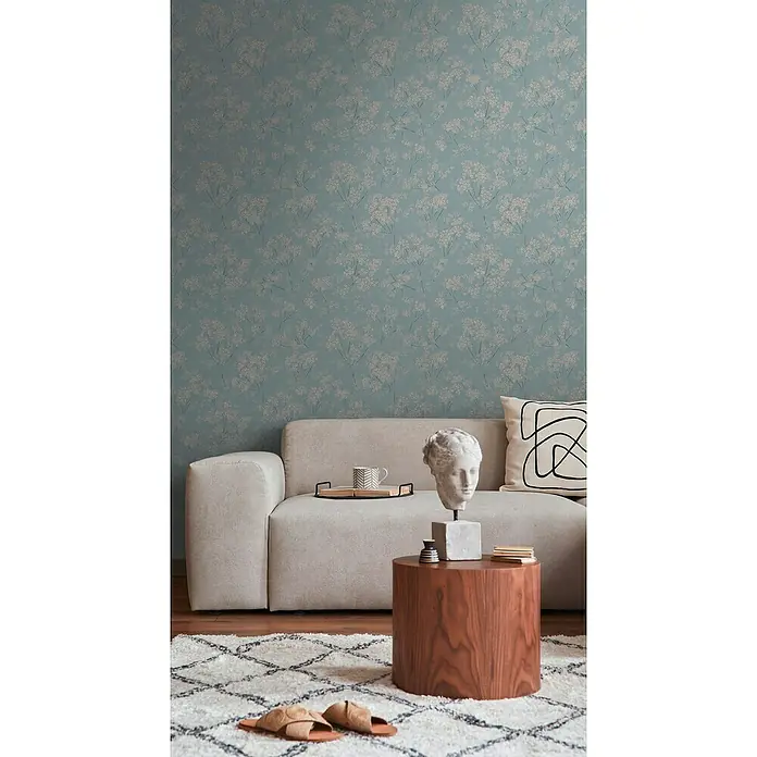 A.S. Création Casual Living Vliestapete Blümchen - Blau/Beige/Türkis, Floral, 10,05 x 0,53 m - Nahaufnahme eines Wohnzimmers mit beigem Sofa, Holztisch und gemusterter Tapete, das ein gemütliches und stilvolles Ambiente schafft.