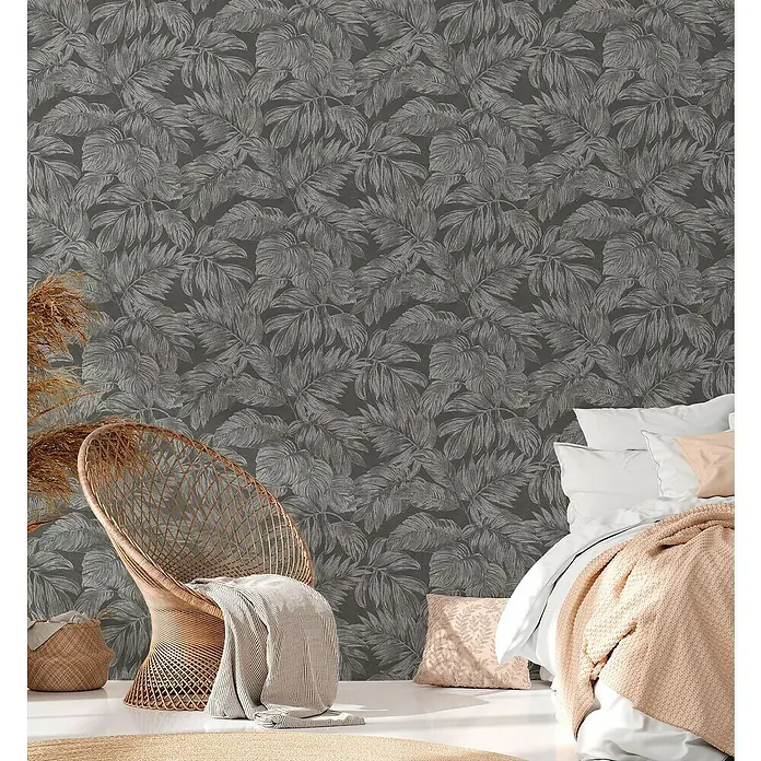 A.S. Création Casual Living Vliestapete - Anthrazit/Grau/Silber, Floral, 10,05 x 0,53 m - Zimmer mit grauer Blättertapete, Korbsessel, beige Decke und Bettwäsche für ein ruhiges Ambiente.