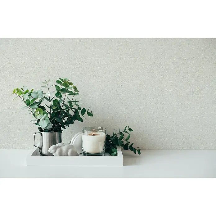 A.S. Création Casual Living Vliestapete - Freundliches Weiß, Uni, 10,05 x 0,53 m - Kerze im Glas, Eukalyptus in einem Becher und eine Hasenfigur auf einem weißen Tablett vor einer hellen Wand.