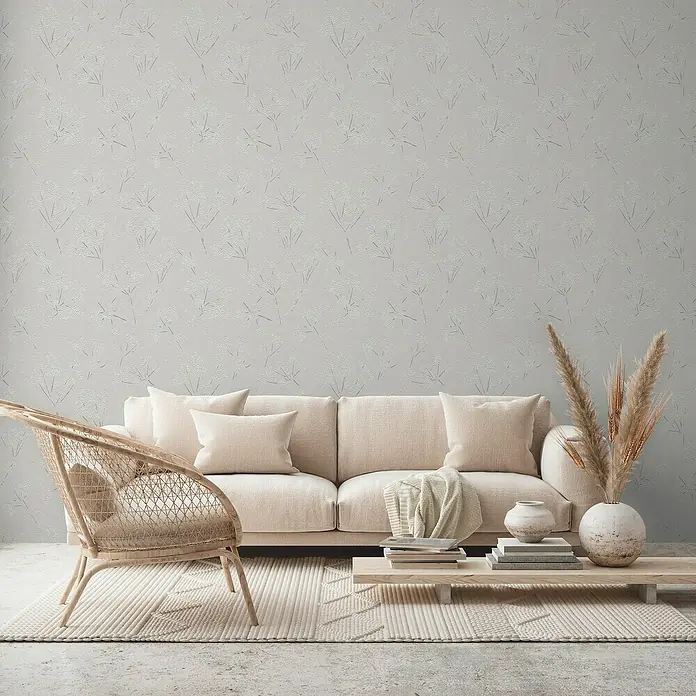 A.S. Création Casual Living Vliestapete Blümchen - Grau/Weiß, Floral, 10,05 x 0,53 m - Wohnzimmer-Interieur mit beigem Sofa, Korb-Sessel, Couchtisch mit Dekorationen und einem Teppich vor einer strukturierten Wand.