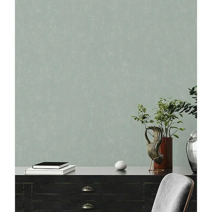 A.S. Création Casual Living Vliestapete - Mintblau, Uni, 10,05 x 0,53 m - Nahaufnahme eines eleganten Interieurs mit stilvollem Schrank, Büchern und dekorativen Elementen vor einer dezenten, texturierten Wand.