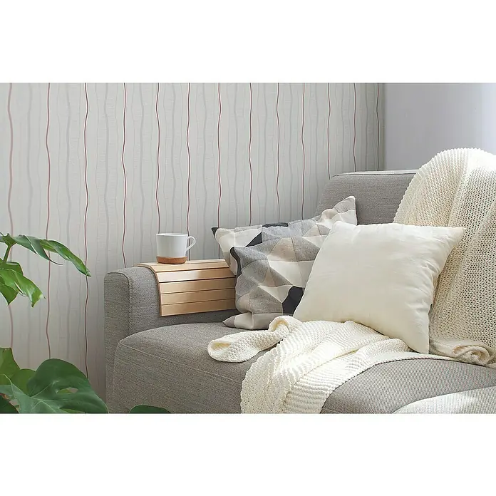 A.S. Création Casual Living Vliestapete - Creme/Rot, Streifen, 10,05 x 0,53 m - Gemütliche Sofaecke mit Kissen und Decke lädt zum Verweilen ein, eine Tasse steht bereit.