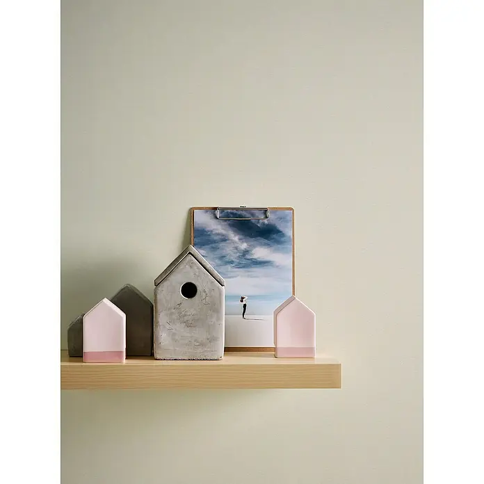 A.S. Création Casual Living Vliestapete - Beigeweiß, Uni, 10,05 x 0,53 m - Dekorative Zementhäuschen und ein Clipboard mit einem Strandbild schmücken das helle Holzregal vor einer dezenten Wand.