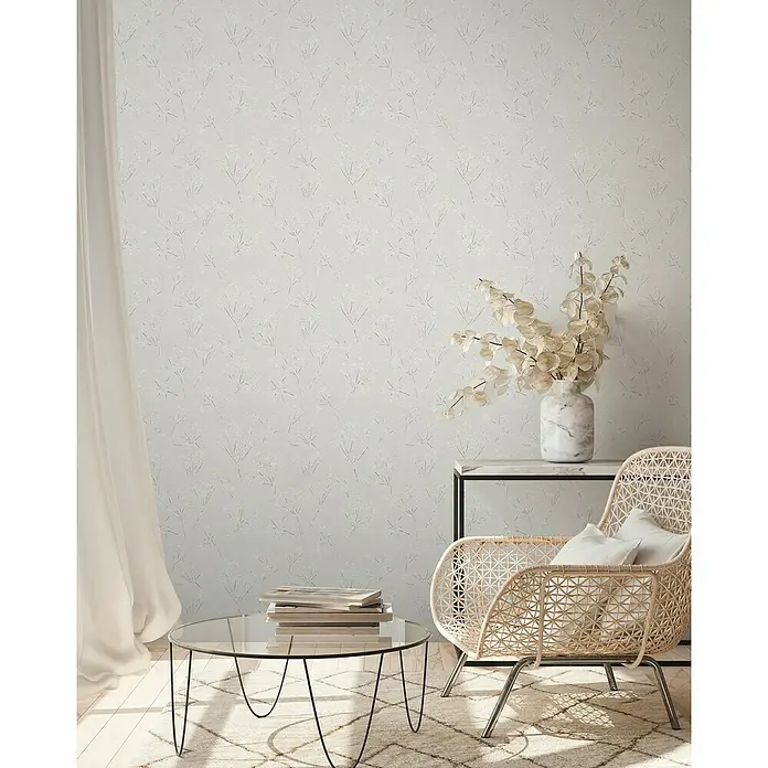 A.S. Création Casual Living Vliestapete Blümchen - Grau/Weiß, Floral, 10,05 x 0,53 m - Nahaufnahme eines eleganten Raumes mit einem Rattansessel, einem Couchtisch aus Glas und einer stilvollen Marmorvase.