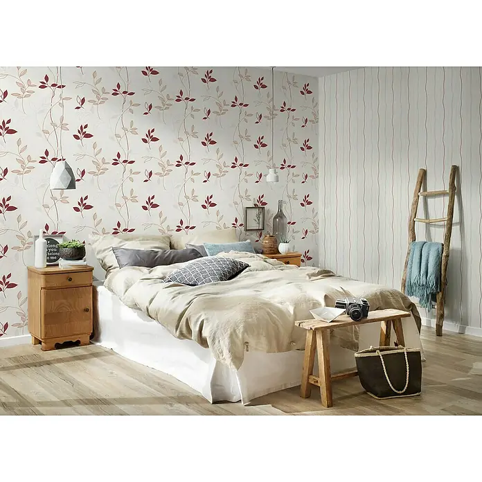 A.S. Création Casual Living Vliestapete Blätter - Creme/Rot/Beige, Floral, 10,05 x 0,53 m - Einladendes Schlafzimmer mit einem bequemen Bett, verziert mit einem attraktiven Blättermuster-Tapete und einem rustikalen Holzleiter-Dekoelement.