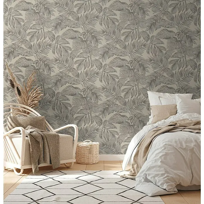 A.S. Création Casual Living Vliestapete - Braun/Grau/Beige, Floral, 10,05 x 0,53 m - Einladendes Schlafzimmer mit Bett, Sessel, Teppich und einer Tapete mit Blattmuster, die eine entspannte Atmosphäre schafft.