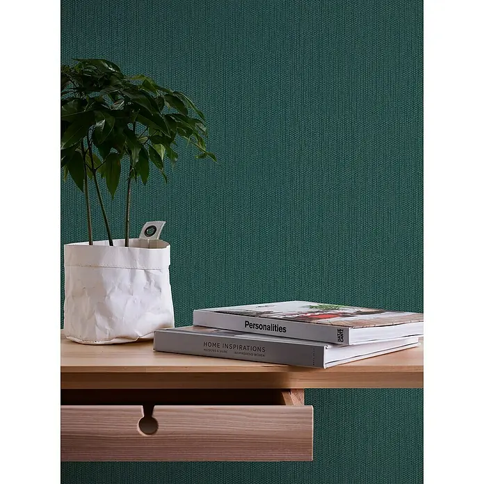 A.S. Création Casual Living Vliestapete Strukturtapete - Grün/Dunkelgrün, Uni, 10,05 x 0,53 m - Nahaufnahme eines Holzschreibtischs mit Topfpflanze und Büchern, die eine warme und einladende Atmosphäre schaffen.