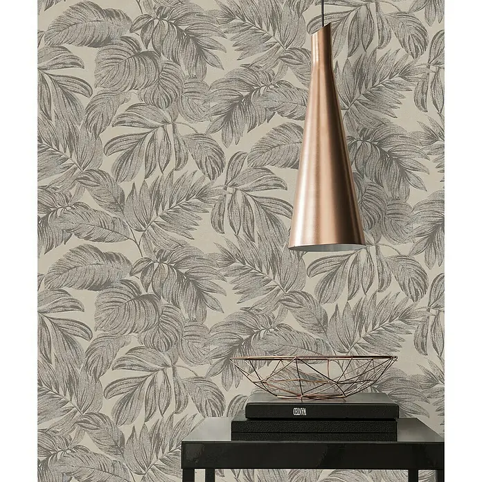 A.S. Création Casual Living Vliestapete - Braun/Grau/Beige, Floral, 10,05 x 0,53 m - Ein stilvolles Interieur mit einer modernen Kupferlampe und einer dekorativen Schale auf einem schwarzen Tisch vor einer Tapete mit Blattmuster.