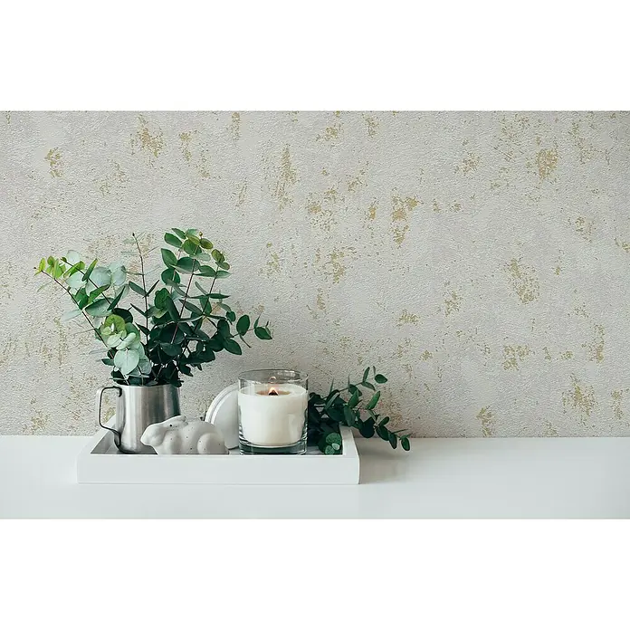 A.S. Création Casual Living Vliestapete Struktur - Grau/Gold/Metallic, Uni, 10,05 x 0,53 m - Ein dekoratives Stillleben mit einem weißen Tablett, einer Kerze, einem silbernen Krug mit Eukalyptus und einer Hasenfigur vor einer strukturierten Wand.