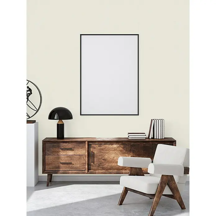 A.S. Création Casual Living Vliestapete - Creme/Weiß, Uni, 10,05 x 0,53 m - Einrichtung mit einem Holzschrank, einer Lampe und einem Sessel, mit einem Bilderrahmen an der Wand.