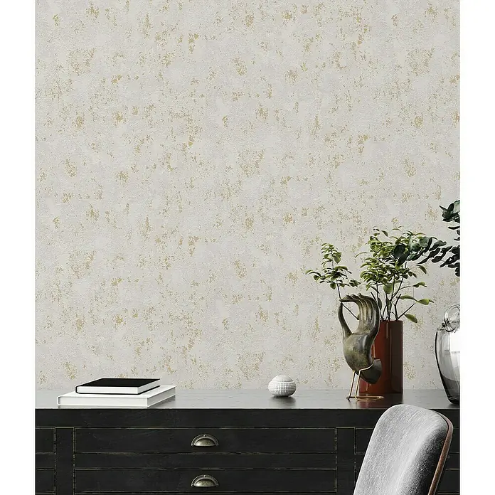 A.S. Création Casual Living Vliestapete Struktur - Grau/Gold/Metallic, Uni, 10,05 x 0,53 m - Nahaufnahme einer stilvollen Kommode mit Dekorationsgegenständen und Büchern vor einer texturierten Wand, die eine elegante Atmosphäre schafft.