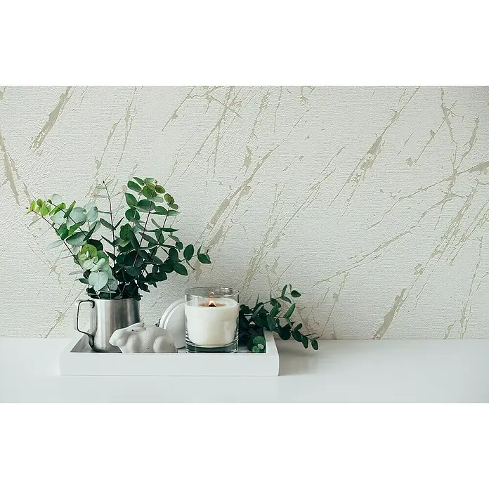 A.S. Création Casual Living Vliestapete Marmor - Weiß/Champagner/Metallic, Steinoptik, 10,05 x 0,53 m - Stillleben mit Eukalyptus in einem Krug, Kerze und Hasenfigur auf einem Tablett vor einer strukturierten Wand.