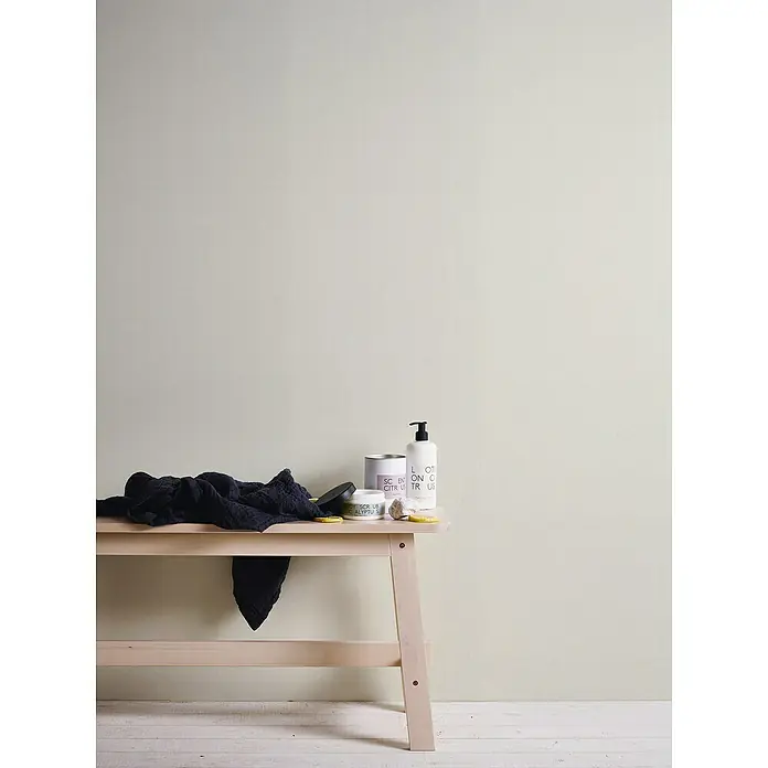 A.S. Création Casual Living Vliestapete Textiloptik - Weiß, Uni, 10,05 x 0,53 m - Dekorative Badezimmer-Szene mit Hautpflegeprodukten, darunter Lotion, Peeling und Handtuch auf einer Holzbank, vor einem neutralen Hintergrund.
