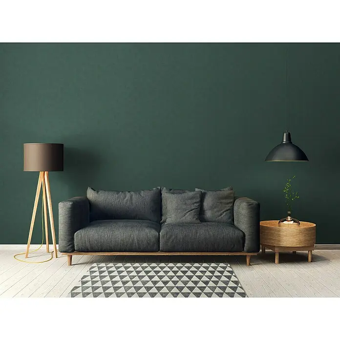 A.S. Création Casual Living Vliestapete - Grün, Uni, 10,05 x 0,53 m - Ein modernes Wohnzimmer mit einem grauen Sofa, einer Stehlampe und einem Beistelltisch unter einer Hängelampe, die eine warme und einladende Atmosphäre schafft.