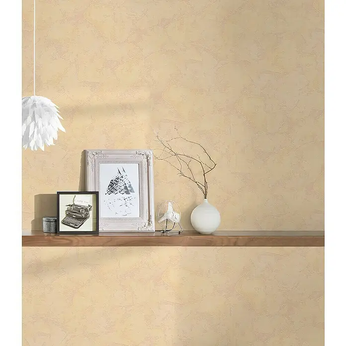 A.S. Création Casual Living Vliestapete - Beige, Uni, 10,05 x 0,53 m - Nahaufnahme eines Regals mit Dekorationsgegenständen, darunter Bilderrahmen, eine Schreibmaschine und eine Vase vor einer beigen Wand.