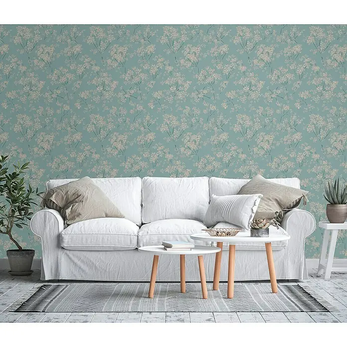 A.S. Création Casual Living Vliestapete Blümchen - Blau/Beige/Türkis, Floral, 10,05 x 0,53 m - Wohnzimmer mit einem weißen Sofa und floral gemusterter Tapete in einem beruhigenden Türkis-Ton, der dem Raum eine frische Note verleiht.