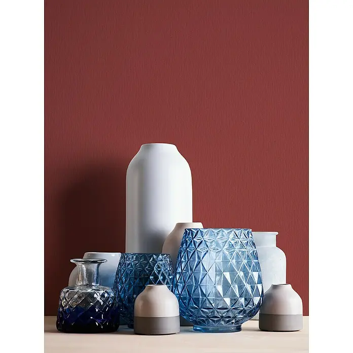 A.S. Création Casual Living Vliestapete - Rot, Uni, 10,05 x 0,53 m - Eine Sammlung von dekorativen Vasen in verschiedenen Formen und Farben, darunter Blau, Weiß und Beige, vor einem roten Hintergrund.