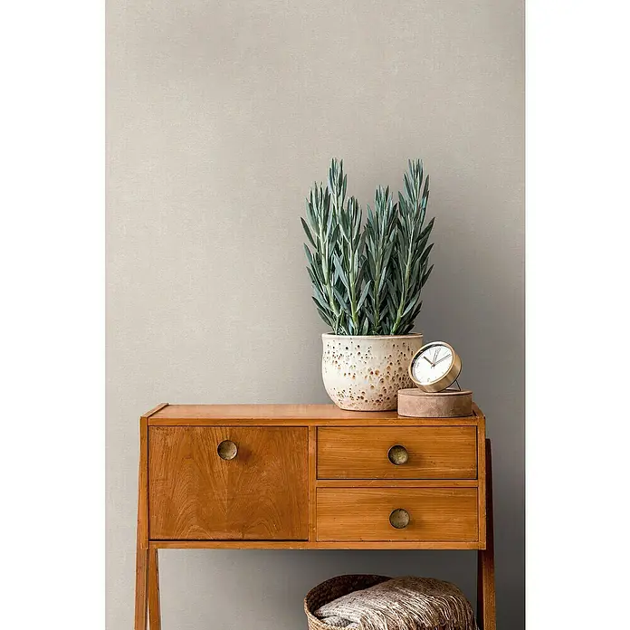 A.S. Création Casual Living Vliestapete - Harmonisches Beige, Uni, 10,05 x 0,53 m - Stilvolles Holz-Sideboard mit Pflanze, Uhr und Korb. Das perfekte Möbelstück für ein gemütliches Zuhause mit praktischem Stauraum.