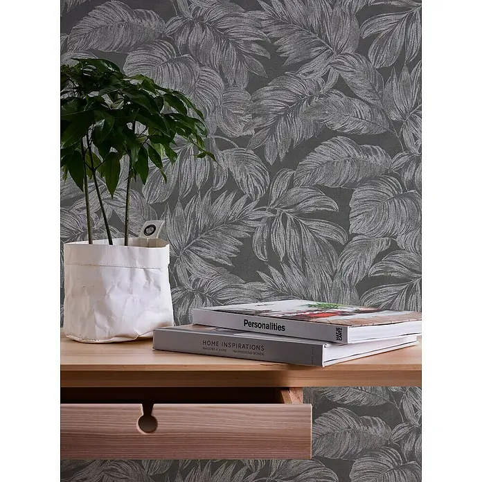A.S. Création Casual Living Vliestapete - Anthrazit/Grau/Silber, Floral, 10,05 x 0,53 m - Bücher und ein Pflanzentopf auf einem Holzschreibtisch mit einer Schublade und einer floralen Tapete im Hintergrund.