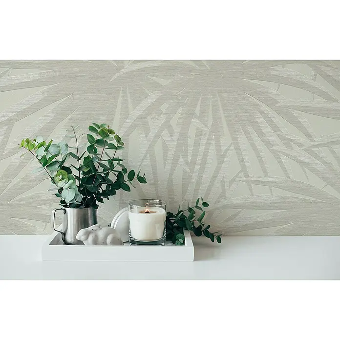 A.S. Création Casual Living Vliestapete Palmenblätter - Creme/Hellgrau, Floral, 10,05 x 0,53 m - Nahaufnahme einer weißen Kerze, eines Blumentopfes mit grünen Blättern und einer dekorativen Hasenfigur auf einem weißen Tablett.
