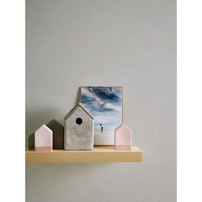A.S. Création Casual Living Vliestapete - Grau/Hellgrau, Uni, 10,05 x 0,53 m - Drei kleine Häuser und eine Fotografie auf einem Regal. Die Häuser sind in Rosa und Grau gehalten, während die Fotografie einen bewölkten Himmel zeigt.