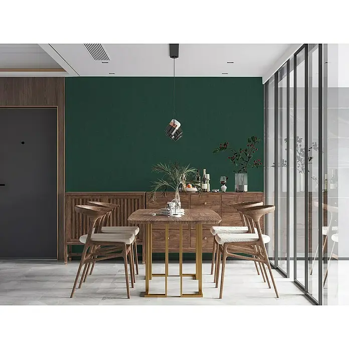 A.S. Création Casual Living Vliestapete - Waldgrün, Uni, 10,05 x 0,53 m - Stilvoller Essbereich mit Holztisch und Stühlen vor einer grünen Wand, akzentuiert durch eine moderne Pendelleuchte.