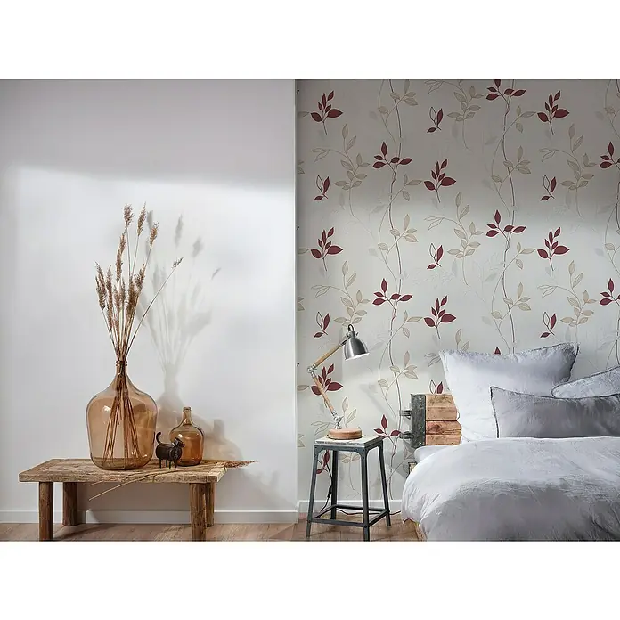 A.S. Création Casual Living Vliestapete Blätter - Creme/Rot/Beige, Floral, 10,05 x 0,53 m - Blick auf ein dekoriertes Schlafzimmer mit großem Glasballon, Tischlampe und einem floralen Tapetenmuster in Rot und Beige.