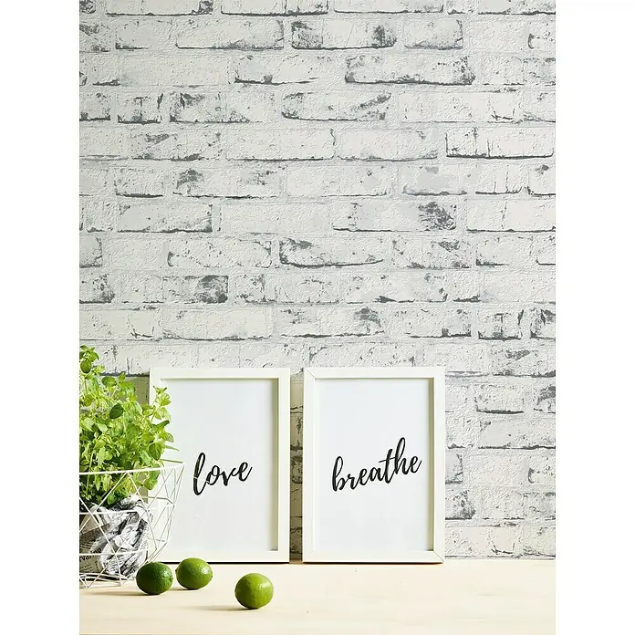 A.S. Création Casual Living Vliestapete New England Klinker - Grau/Anthrazit, Steinoptik, 10 x 0,53 m - Das Bild zeigt dekorative Kunstdrucke mit den Aufschriften "Liebe" und "Atmen", umgeben von einer Pflanze und Limetten vor einer Backsteinmauer.