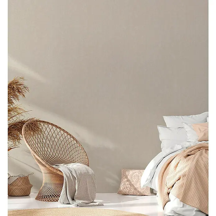 A.S. Création Casual Living Vliestapete - Harmonisches Beige, Uni, 10,05 x 0,53 m - Behagliches Schlafzimmer mit Rattan-Sessel, Decken und Kissen in sanften Farben. Das helle Interieur strahlt Ruhe und Komfort aus.