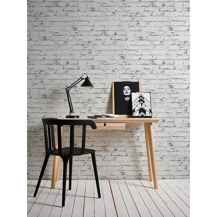 A.S. Création Casual Living Vliestapete New England Klinker - Grau/Anthrazit, Steinoptik, 10 x 0,53 m - Schwarzer Stuhl an einem hellen Holzschreibtisch mit Lampe und Bilderrahmen vor einer weißen Ziegelwand.