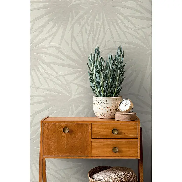 A.S. Création Casual Living Vliestapete Palmenblätter - Creme/Hellgrau, Floral, 10,05 x 0,53 m - Ein dekoratives Holzsideboard mit Topfpflanze und Vintage-Uhr, perfekt für ein stilvolles Zuhause.