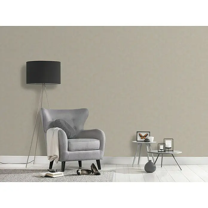 A.S. Création Casual Living Vliestapete - Grau/Beige, Uni, 10,05 x 0,53 m - Einrichtungsszene mit einem grauen Sessel, Stehlampe und Beistelltischen vor einer strukturierten Wand. Stilvolle und gemütliche Atmosphäre.