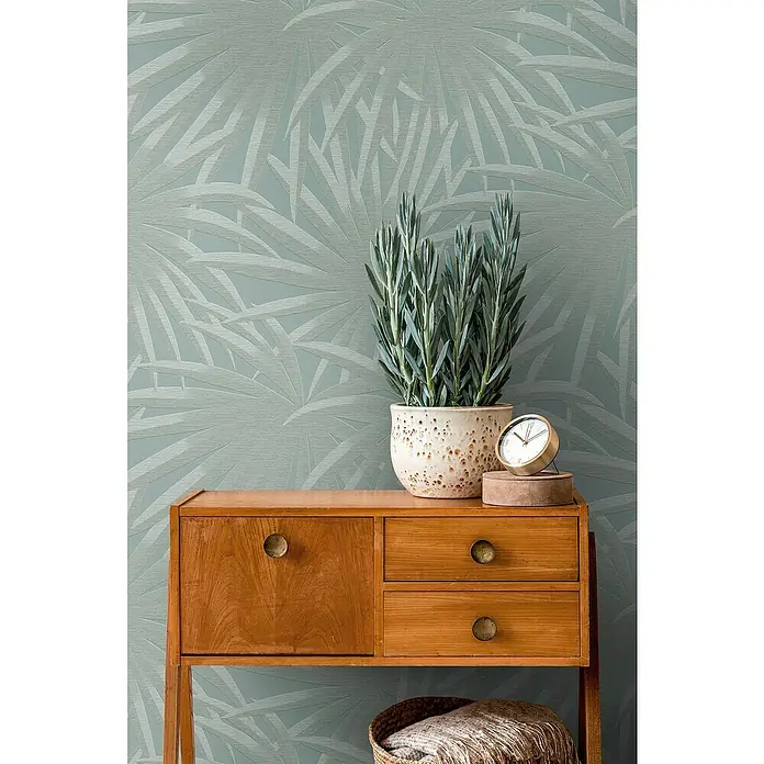 A.S. Création Casual Living Vliestapete Palmenblätter - Blau/Mint, Floral, 10,05 x 0,53 m - Ein Schrank mit einer Pflanze und einer Uhr darauf. Das Möbelstück ist aus Holz und hat Schubladen und eine Tür. Die Pflanze ist in einem Topf.