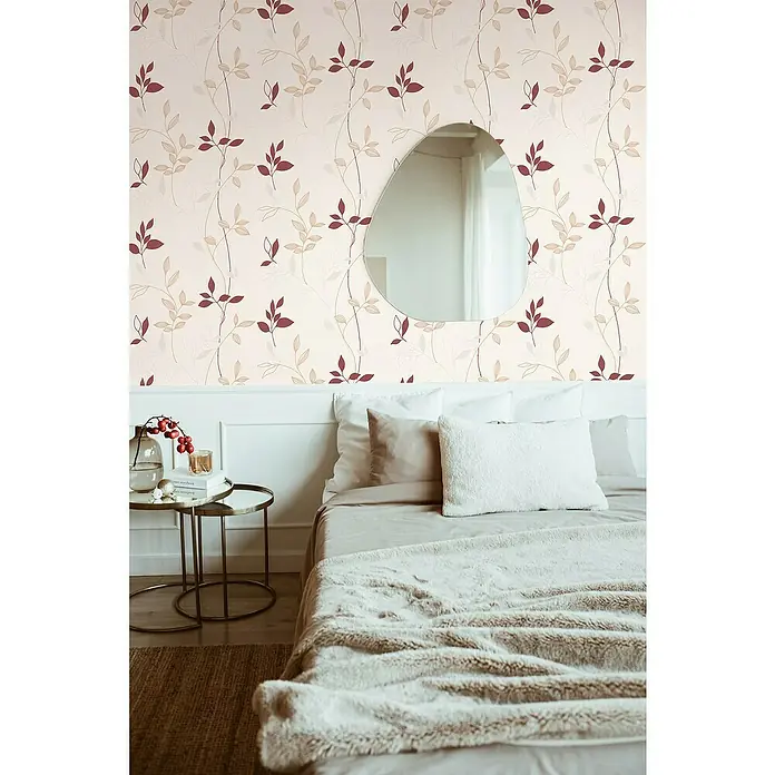 A.S. Création Casual Living Vliestapete Blätter - Creme/Rot/Beige, Floral, 10,05 x 0,53 m - Schlafzimmerdekor mit einem Spiegel an einer floral gemusterten Wand und einem Bett mit weicher Decke und Kissen.