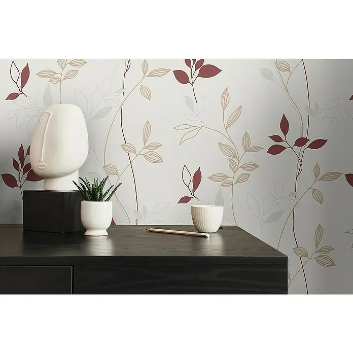 A.S. Création Casual Living Vliestapete Blätter - Creme/Rot/Beige, Floral, 10,05 x 0,53 m - Nahaufnahme eines stilvollen Interieurs mit einer weißen Gesichtsstatue, einer kleinen Sukkulente und einem schlichten Bleistift auf einer dunklen Kommode.