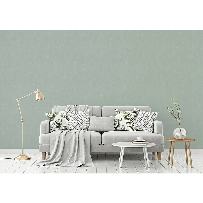 A.S. Création Casual Living Vliestapete - Mintblau, Uni, 10,05 x 0,53 m - Modernes Wohnzimmer mit grauem Sofa, Kissen mit Blattmuster und geometrischen Mustern, ergänzt durch eine Stehlampe und Beistelltische.