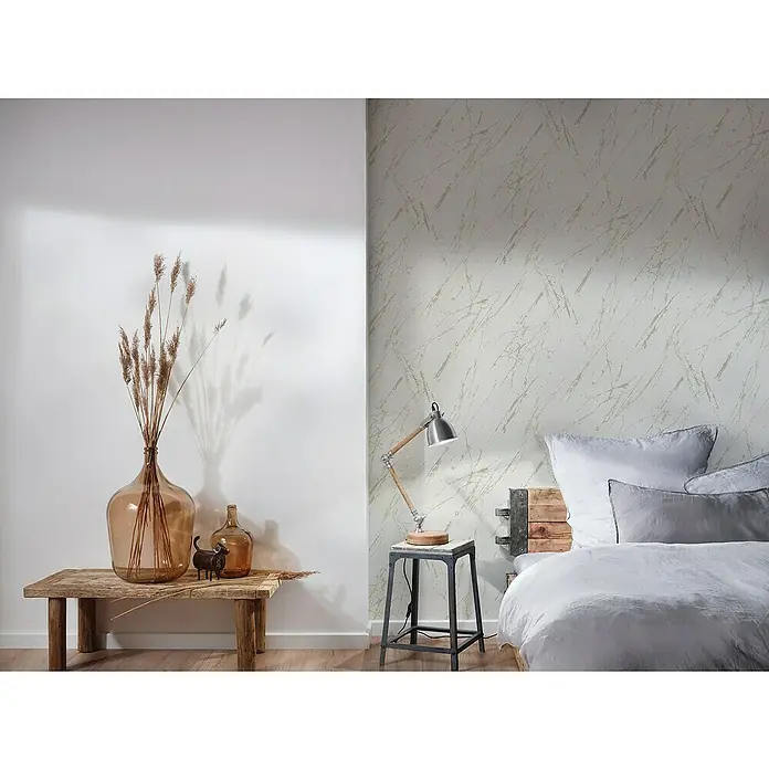 A.S. Création Casual Living Vliestapete Marmor - Weiß/Champagner/Metallic, Steinoptik, 10,05 x 0,53 m - Nahaufnahme von Dekorationsprodukten, darunter eine Vase, eine Tischlampe und eine Bettwäschegarnitur, die ein raffiniertes und doch gemütliches Ambiente schaffen.