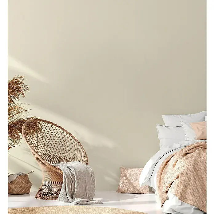 A.S. Création Casual Living Vliestapete - Beigeweiß, Uni, 10,05 x 0,53 m - Ein gemütliches Schlafzimmer mit einem Rattansessel, weichen Textilien und einem runden Teppich, das zum Entspannen einlädt.