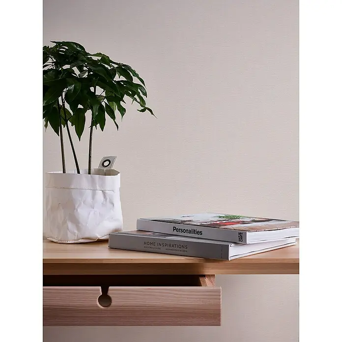 A.S. Création Casual Living Vliestapete Textilstruktur - Cremeweiß, Uni, 10,05 x 0,53 m - Nahaufnahme eines Tisches mit Pflanze, Büchern und einer Schublade. Das schlichte Design und die natürlichen Elemente schaffen eine ruhige Atmosphäre.