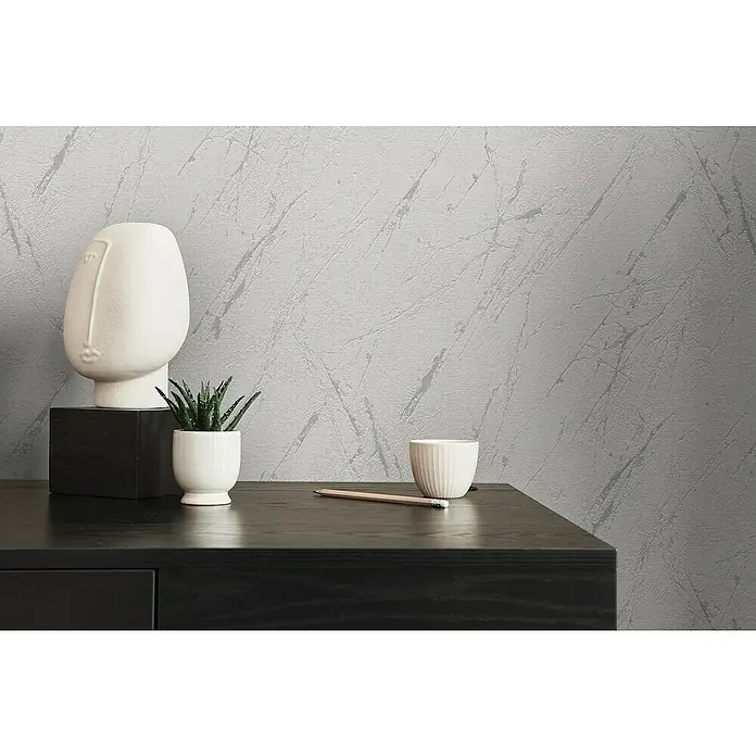 A.S. Création Casual Living Vliestapete Marmor - Silbergrau-Metallic, Steinoptik, 10,05 x 0,53 m - Nahaufnahme einer modernen Tischdekoration mit einer dekorativen Gesichtsstatue, einer Sukkulente und einer minimalistischen Tasse.