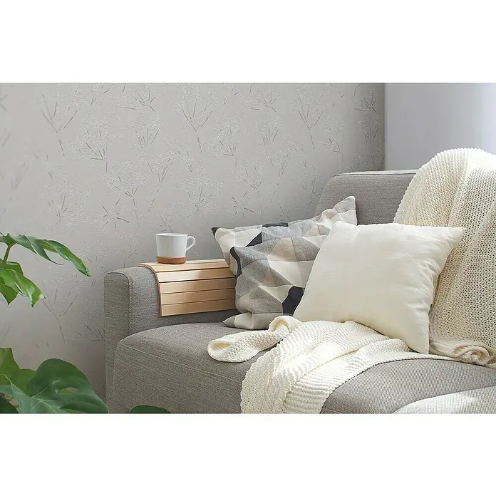 A.S. Création Casual Living Vliestapete Blümchen - Grau/Weiß, Floral, 10,05 x 0,53 m - Gemütliche Sofaecke mit Kaffeetasse, Zierkissen und einer hellen Strickdecke auf einem grauen Sofa, die zum Verweilen einlädt.