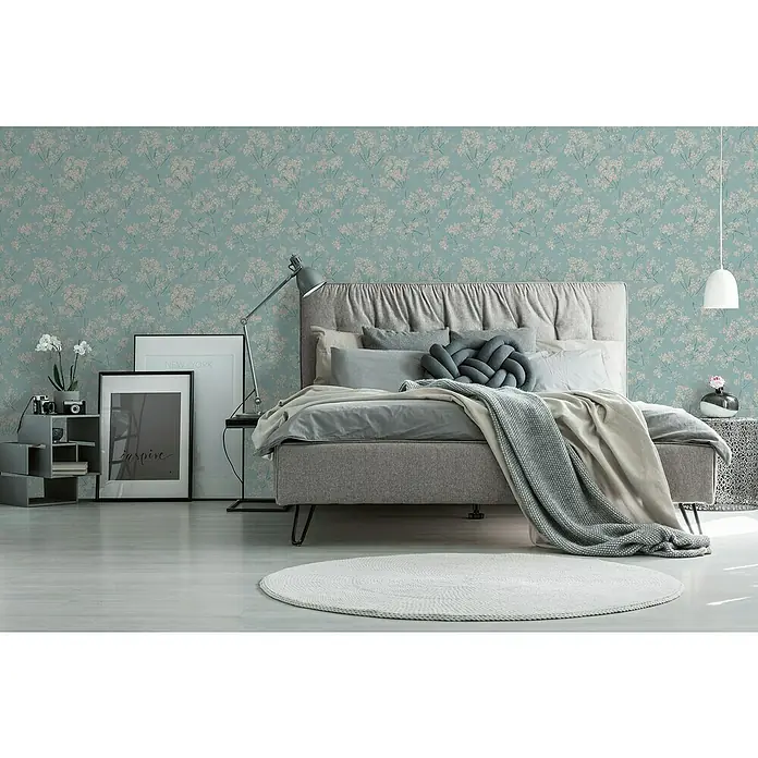A.S. Création Casual Living Vliestapete Blümchen - Blau/Beige/Türkis, Floral, 10,05 x 0,53 m - Elegantes Schlafzimmer mit gemusterten Tapeten. Das harmonische Design umfasst ein graues Bett, einen runden Teppich und eine moderne Lampe für stilvolles Wohnen.