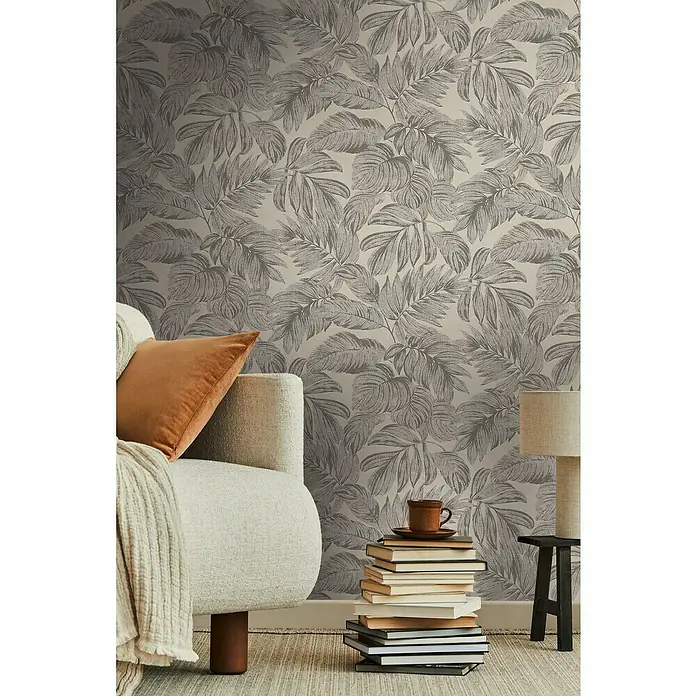 A.S. Création Casual Living Vliestapete - Braun/Grau/Beige, Floral, 10,05 x 0,53 m - Nahaufnahme einer Wand mit tropischem Blättertapetenmuster, die eine gemütliche Atmosphäre in einem Wohnraum erzeugt.