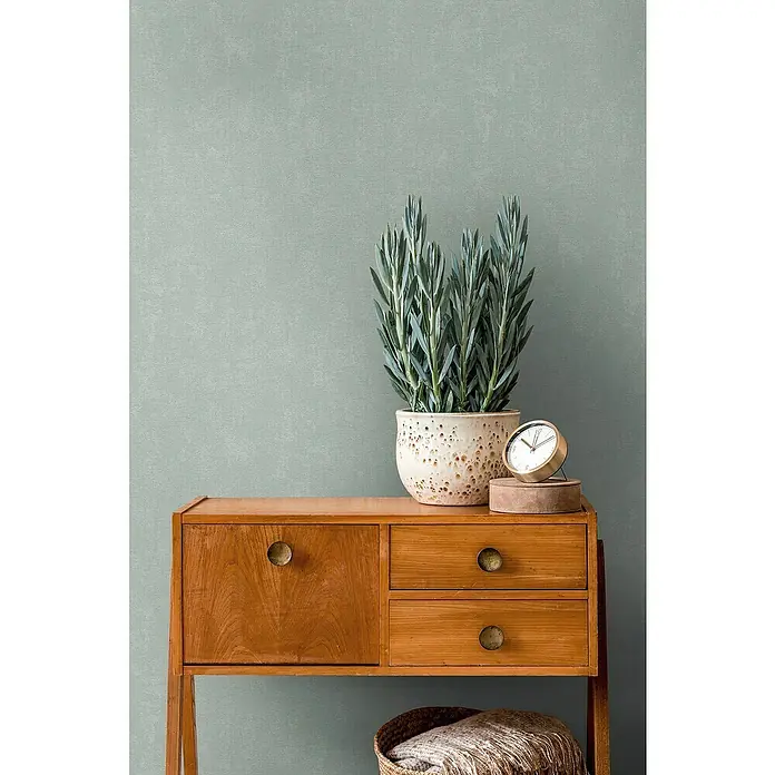 A.S. Création Casual Living Vliestapete - Mintblau, Uni, 10,05 x 0,53 m - Eine stilvolle Kommode aus Holz mit einem dekorativen Topf und einer Uhr, die eine warme und einladende Atmosphäre schafft.