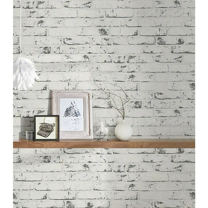 A.S. Création Casual Living Vliestapete New England Klinker - Grau/Anthrazit, Steinoptik, 10 x 0,53 m - Detailaufnahme einer Wand mit weißer Ziegelsteintapete, verziert mit Regalelementen und Dekorationsgegenständen.